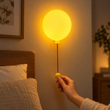 Hand operating the pull cord on a wall-mounted balloon night light